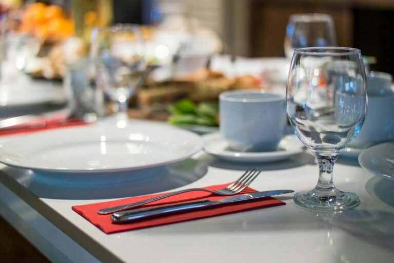 Análisis de costos y rentabilidad en restaurantes - Close-up of an elegant dining table set with glassware, silverware, and red napkins in a restaurant setting.